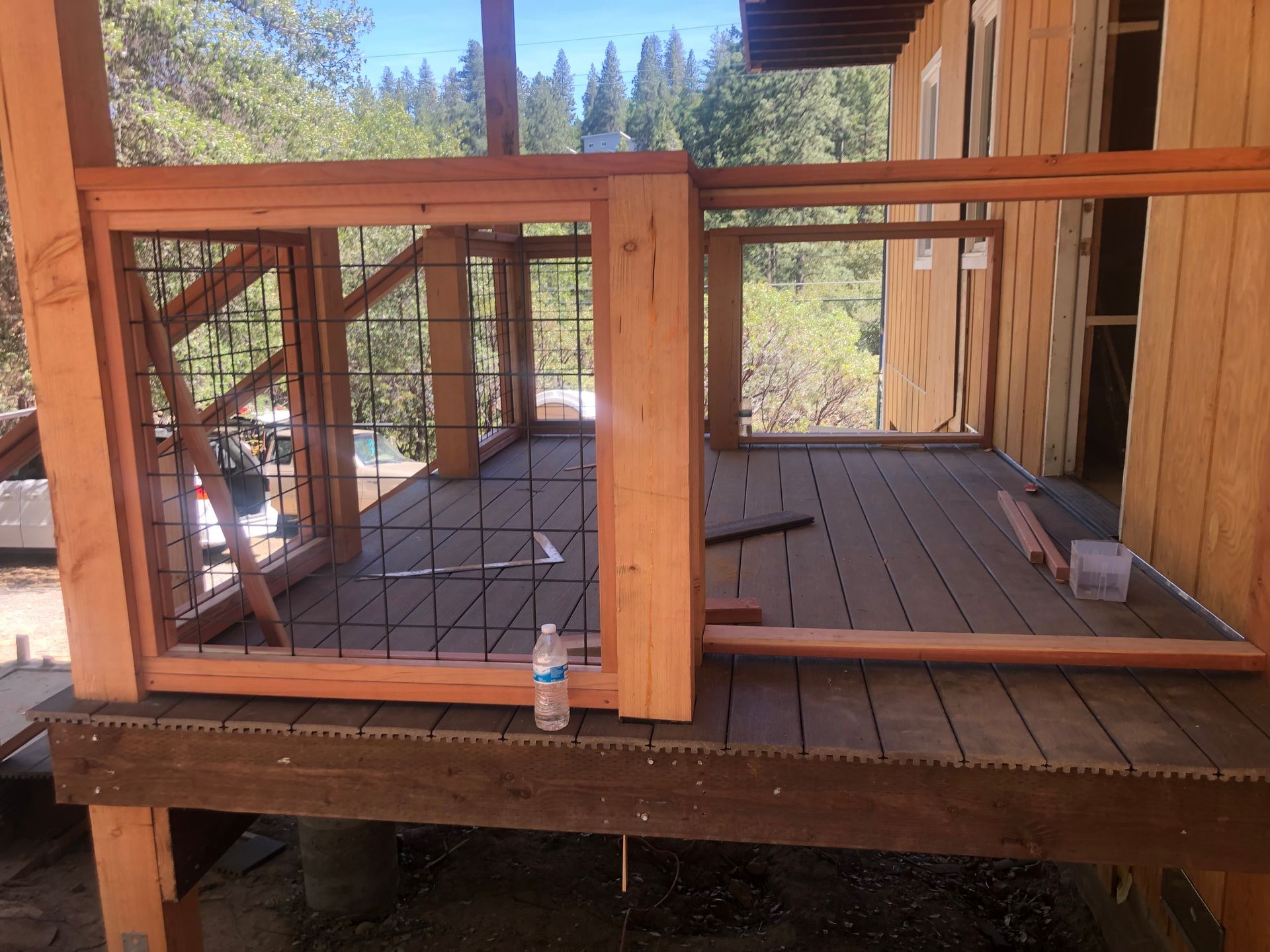 A wood deck under construction, featuring a railing frame with wire mesh panels and a water bottle on the floor.