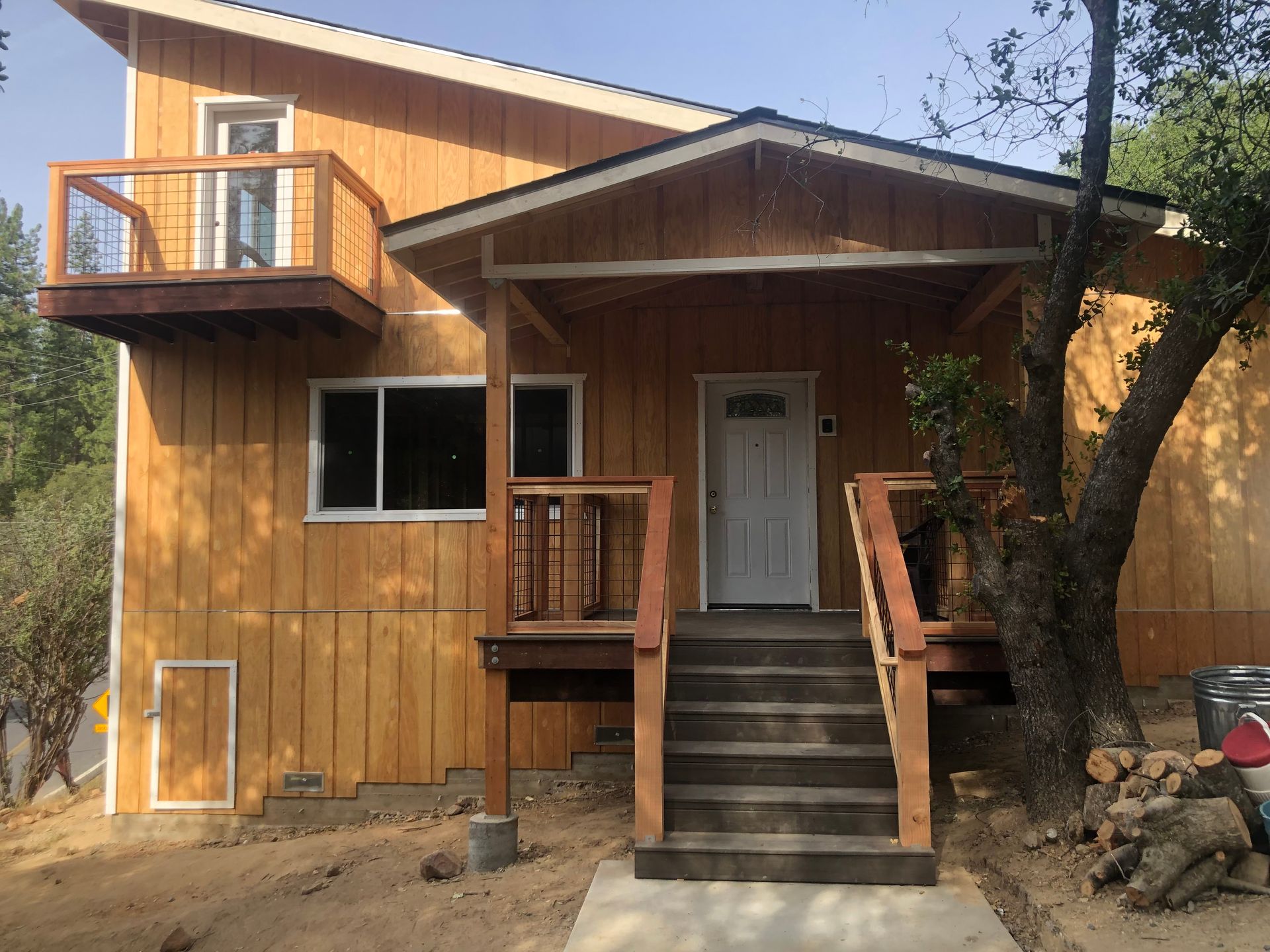 Two-story house with natural wood siding, a front porch with stairs, and an upper-level balcony.