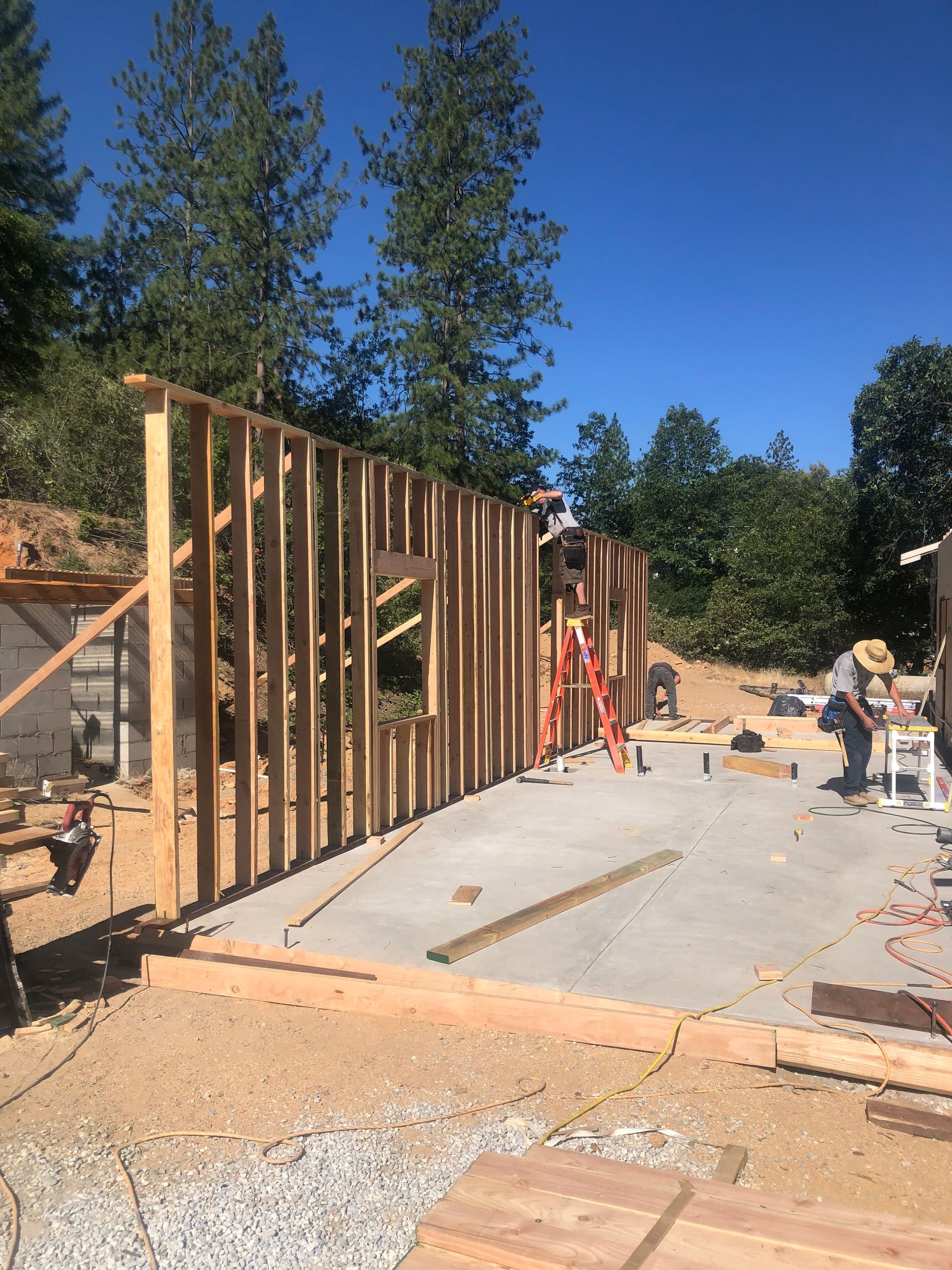 Construction workers framing a wooden wall on a concrete foundation at an outdoor building site.