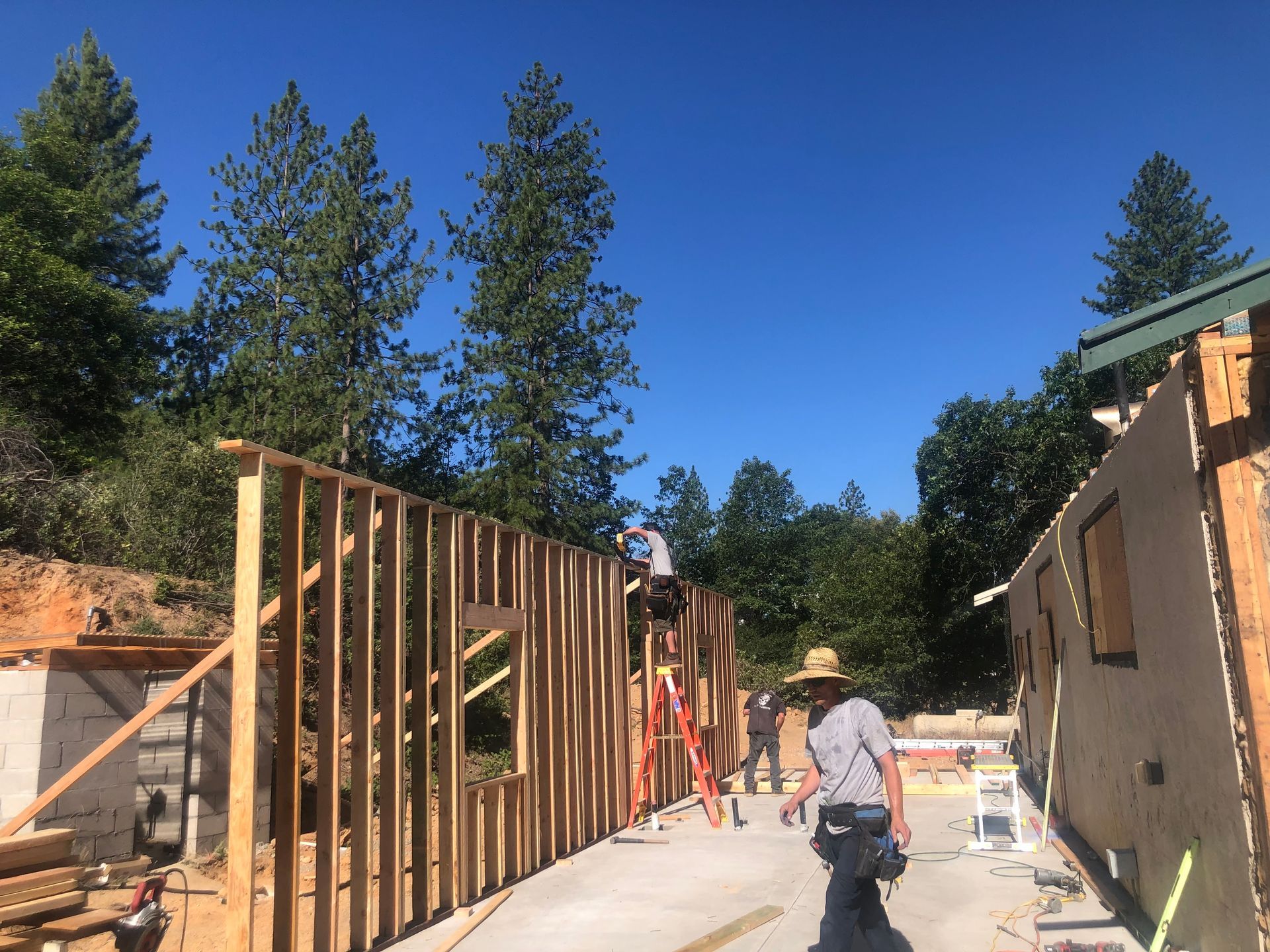 Construction workers frame the exterior walls of a building on a sunny day at a residential work site.