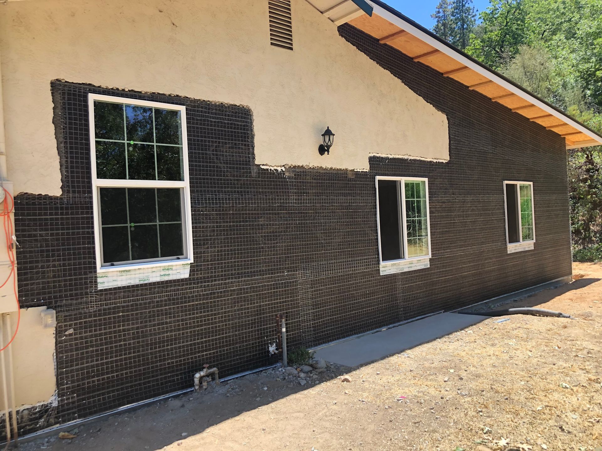 Exterior view of a house wall undergoing renovation, featuring black metal lath installed over the unfinished surface.