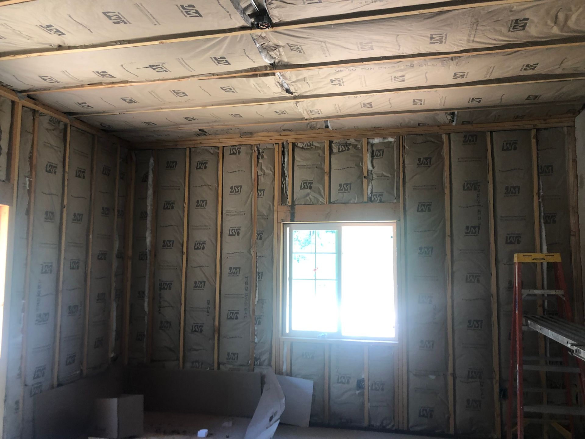 An unfinished room with exposed wooden wall studs and ceiling joists, insulated with kraft-faced fiberglass batts.