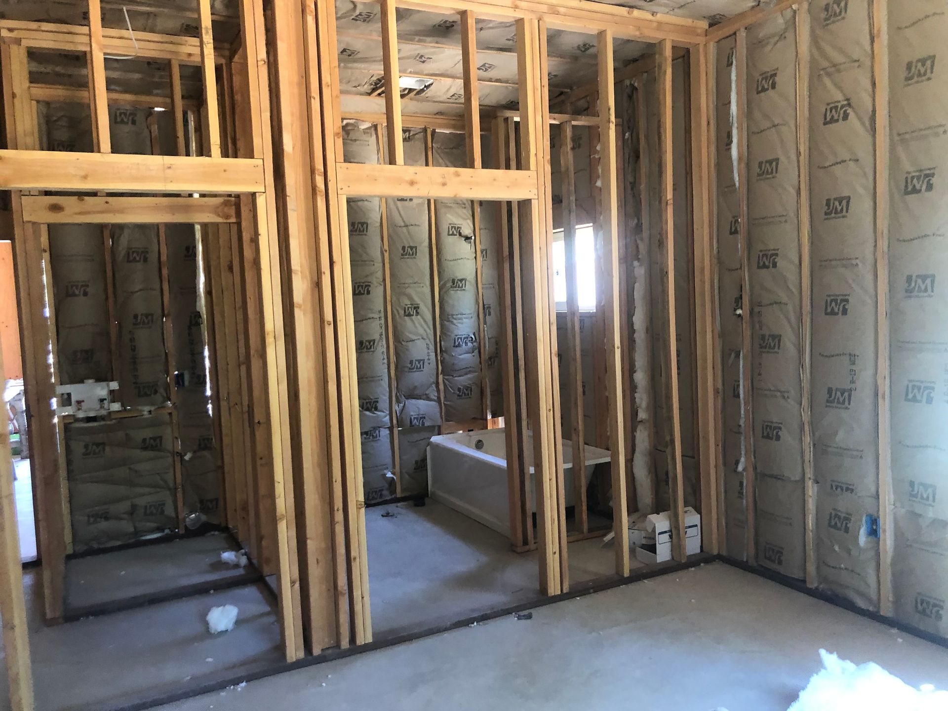 Unfinished bathroom interior showing wood wall framing and insulation batts around a bathtub and shower stall space.