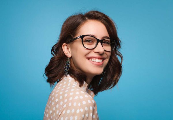 Smiling person with glasses and shoulder-length brown hair against a blue background