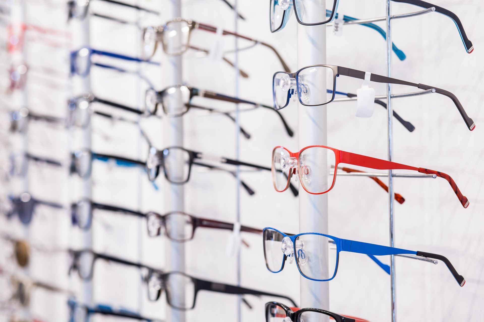 Rows of eyeglasses on display, with red and blue frames on a wall rack