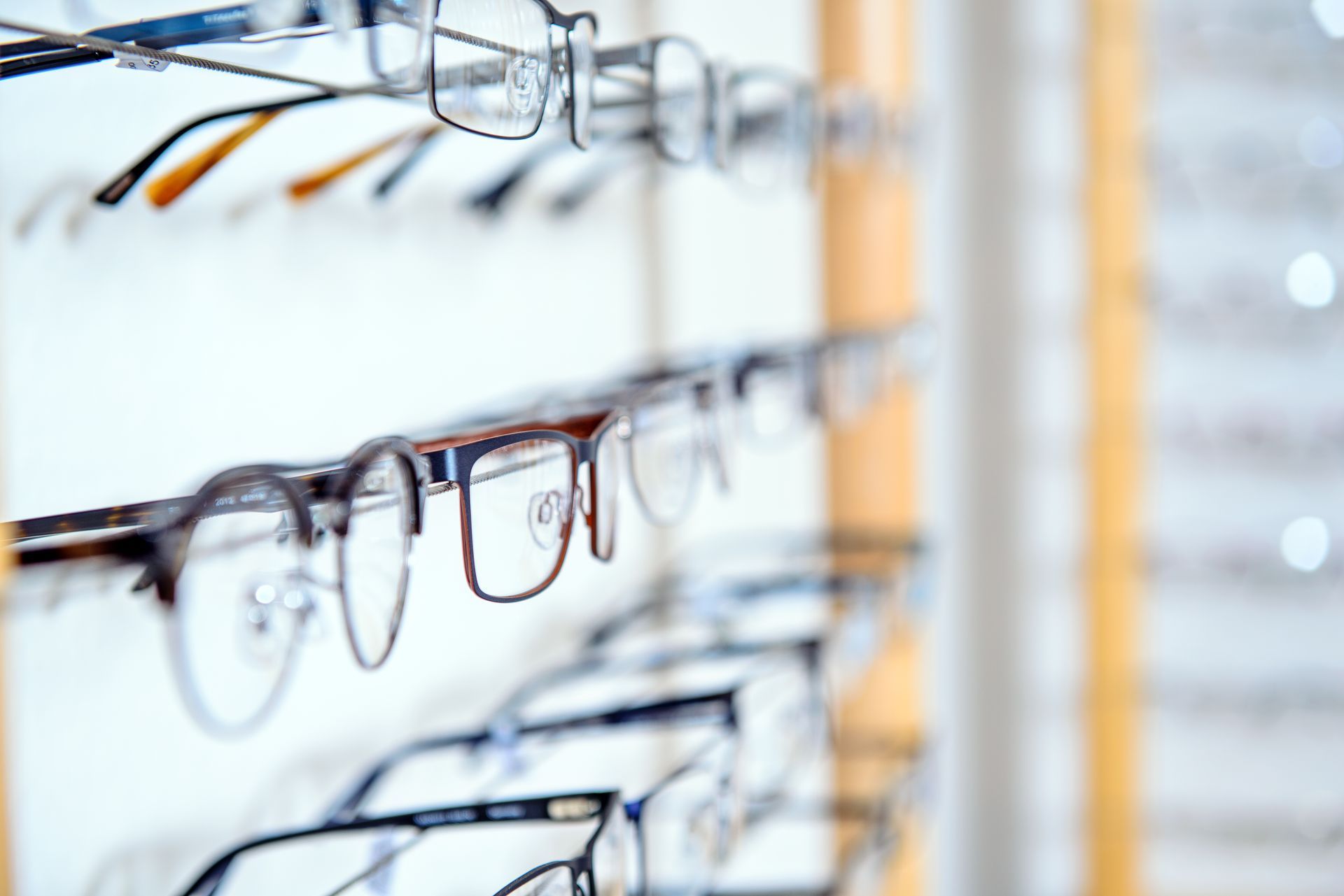 Eyeglasses displayed on a rack in an optical store, with rows of frames in focus and blur.