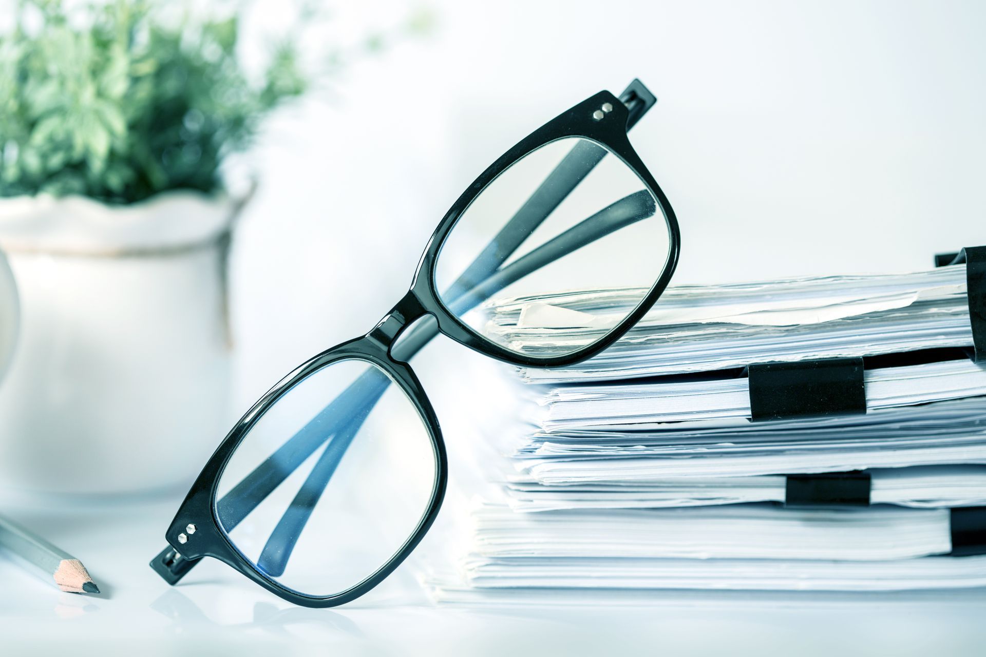 Black eyeglasses resting on a stack of papers beside a pencil