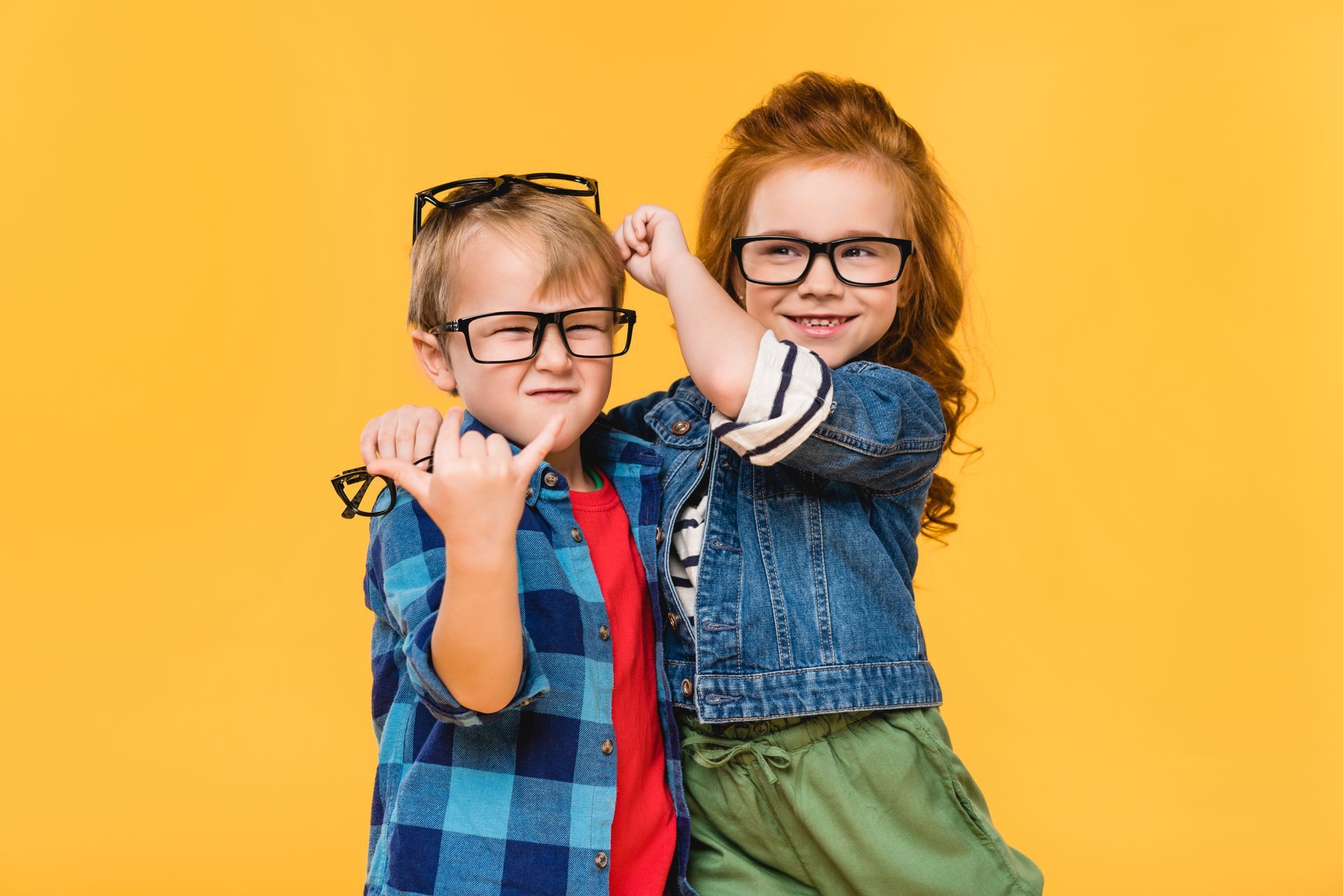 Two children wearing glasses posing playfully against a bright yellow background