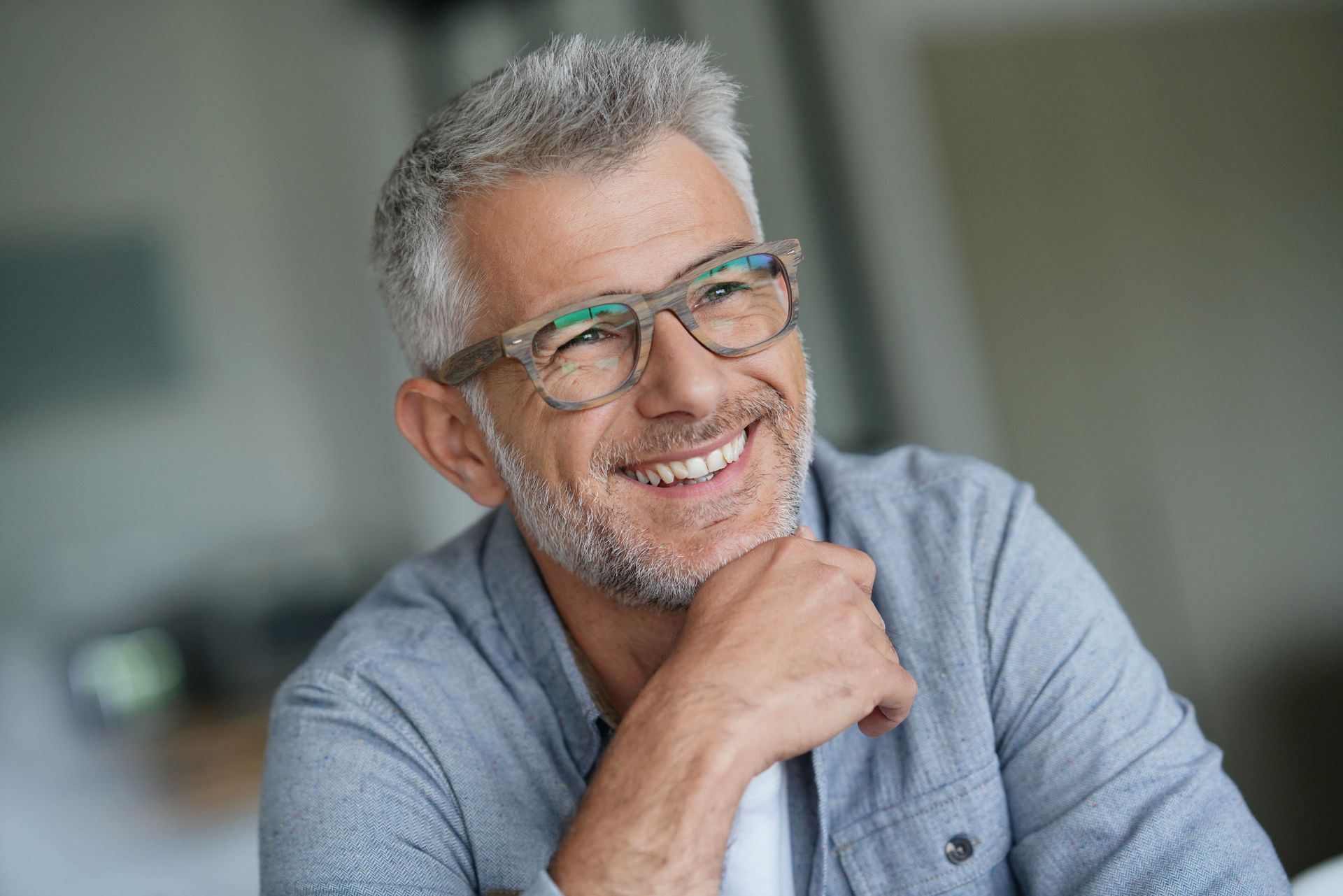 Smiling man with glasses resting his chin on his hand in a bright indoor setting