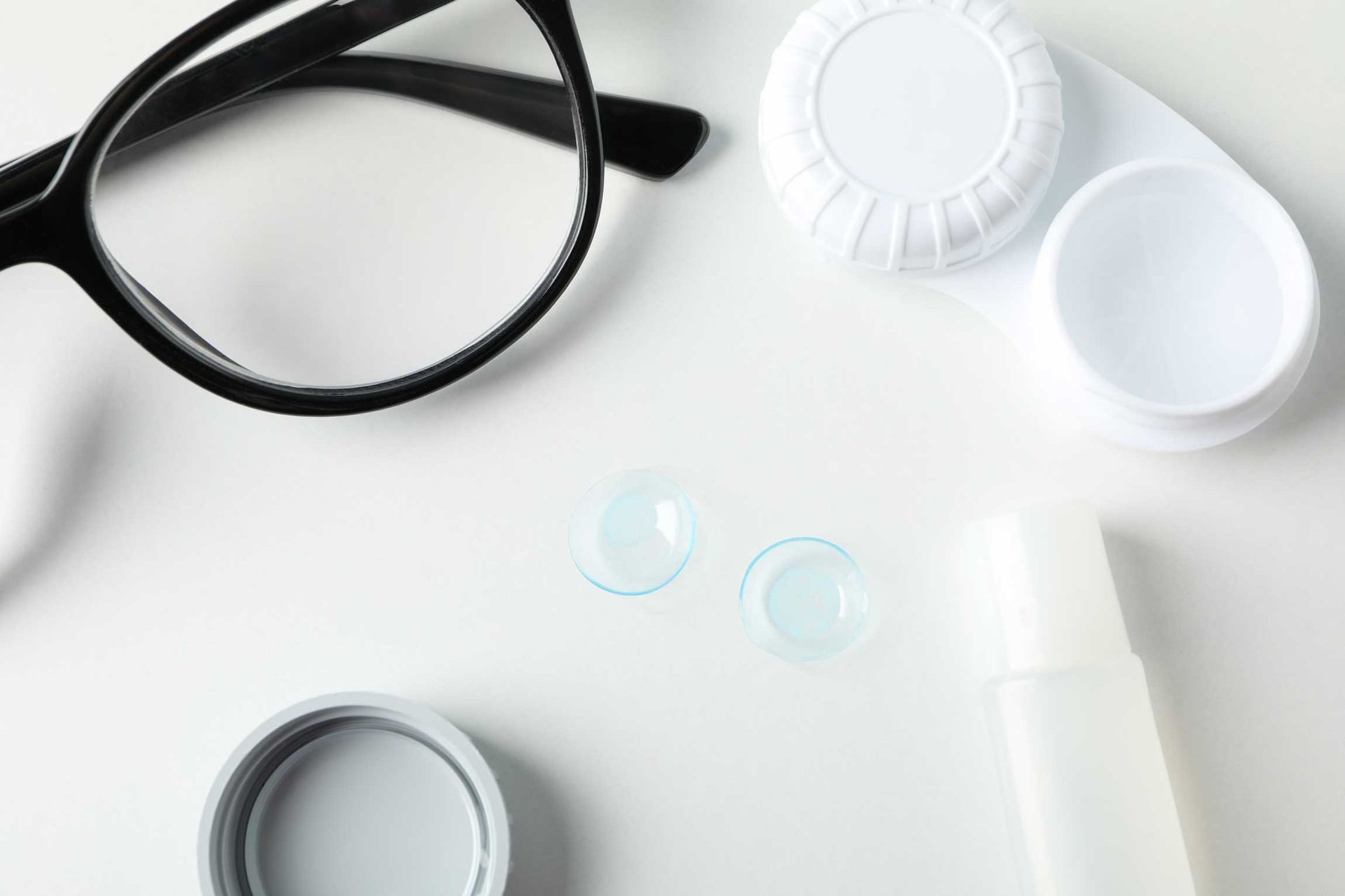 Black eyeglasses and contact lens supplies arranged on a white surface
