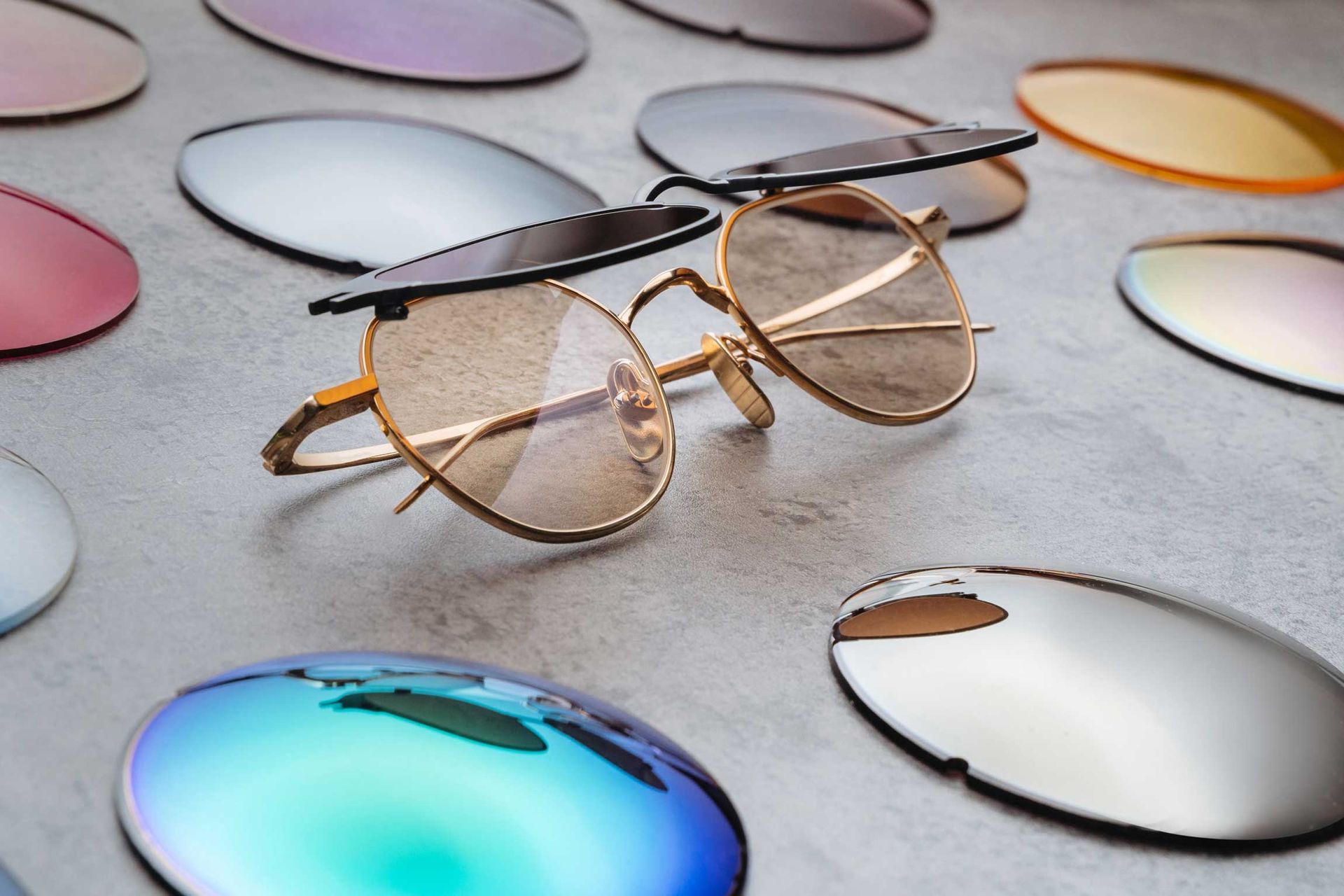 Round eyeglasses on a gray surface surrounded by colorful reflective lenses