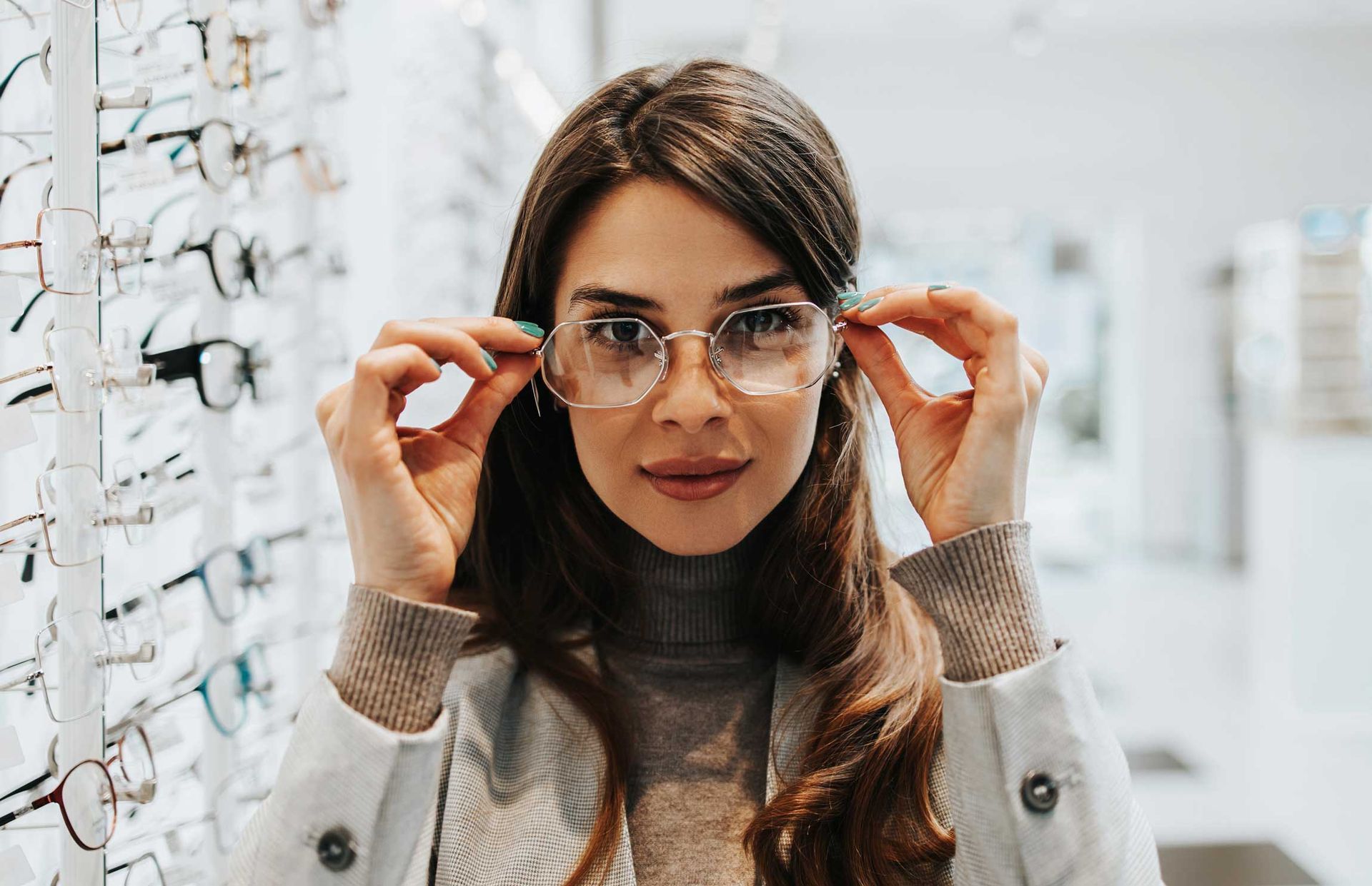 Woman adjusting eyeglasses in an optical store, with shelves of glasses behind her.