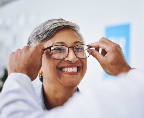 Smiling person adjusting glasses in a bright office setting Smiling person adjusting eyeglasses in a bright room
