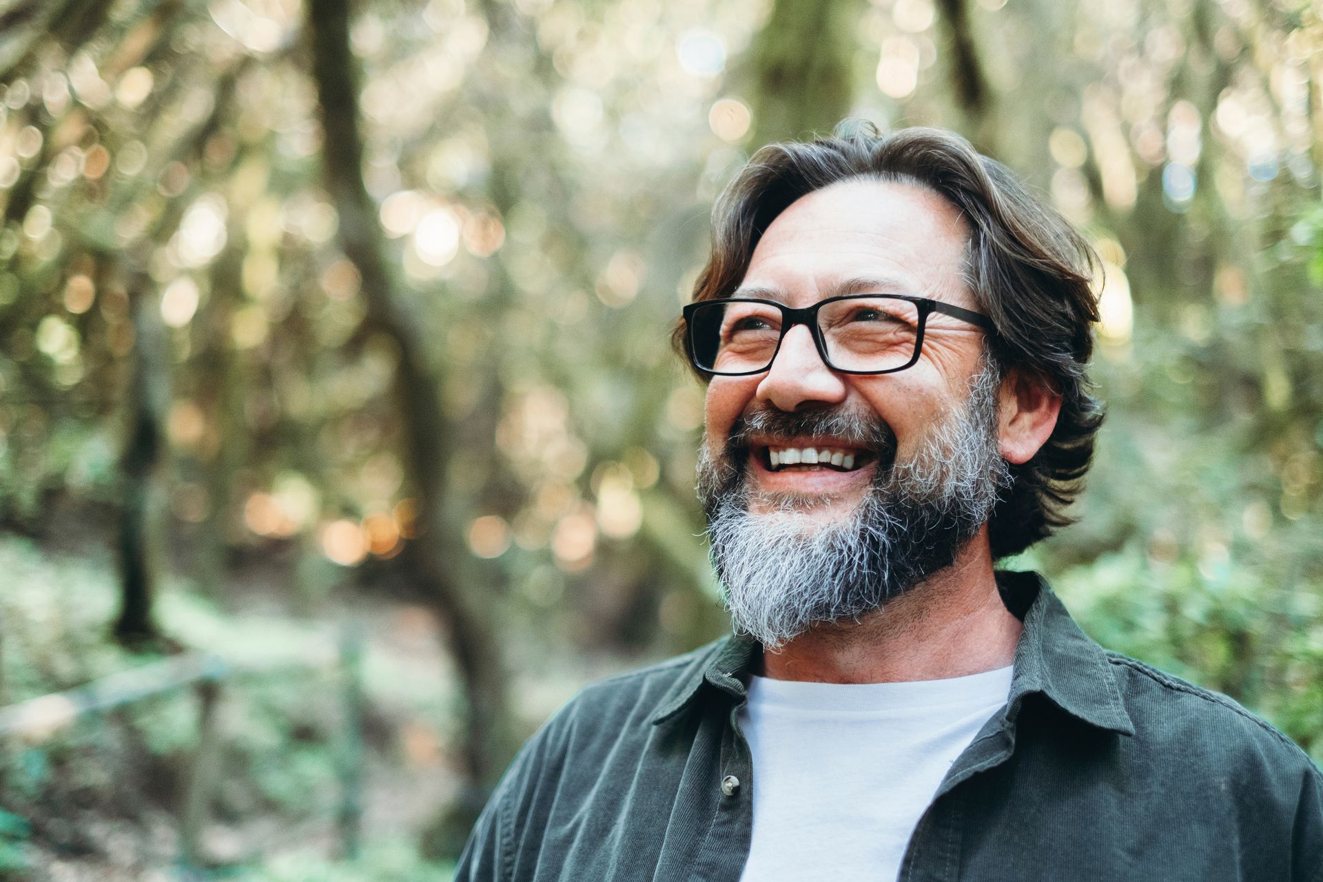 Smiling bearded man with glasses outdoors in a wooded setting