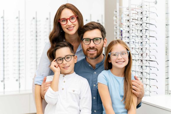 Family posing in an eyeglasses store, smiling beside display racks of frames