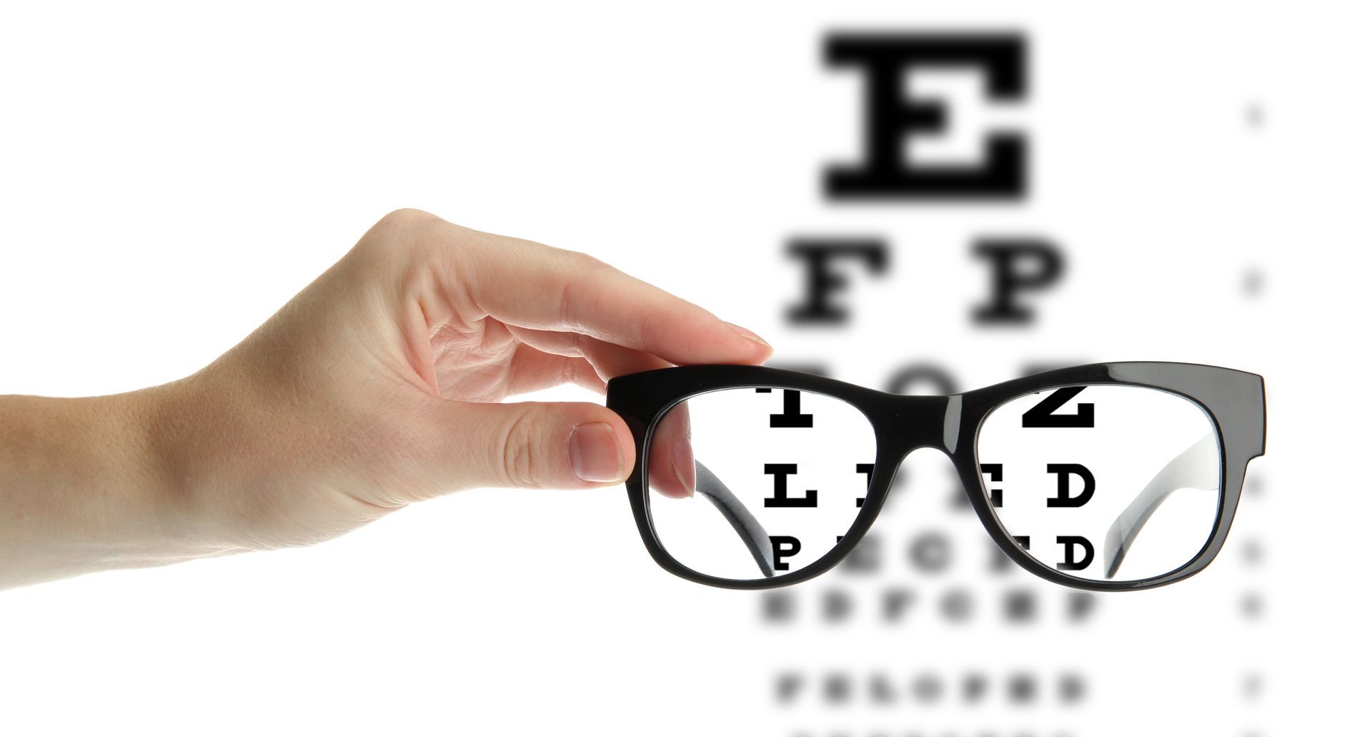 Hand holding eyeglasses in front of an eye chart on a white background