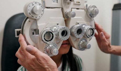 Person having an eye exam with a phoropter at an optometrist’s office Eye exam with phoropter held in front of a patient’s face by an optometrist