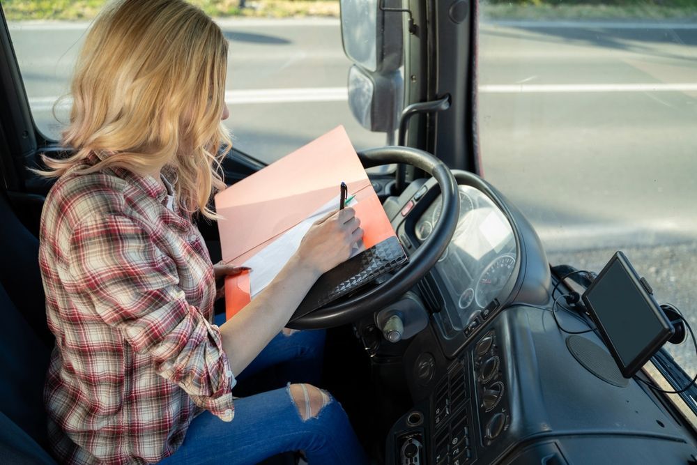 Person in a plaid shirt reading a pink folder while seated at a bus driver’s seat