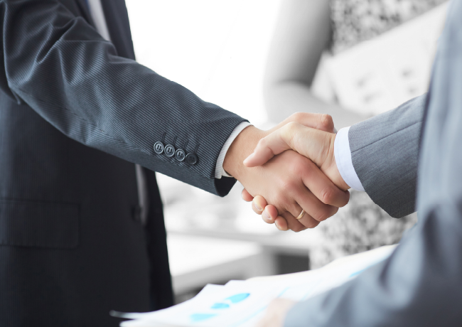 Two people in suits shaking hands, possibly after a business deal.