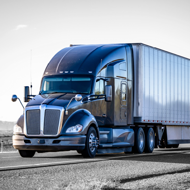 Black semi-truck hauling a trailer on a highway under a bright sky.