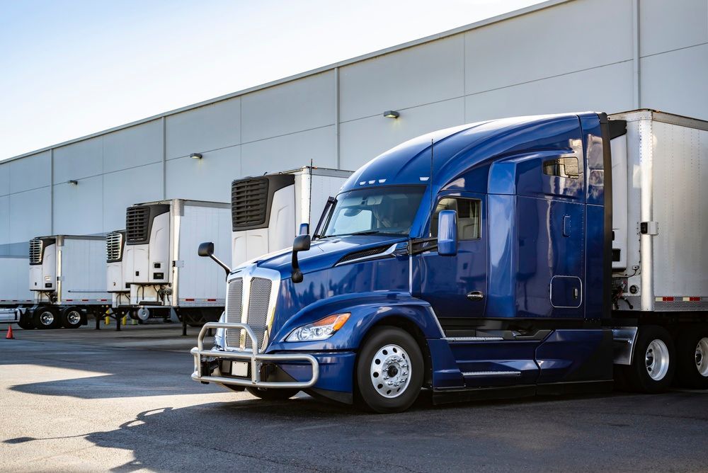 Blue semi-truck parked at a loading dock beside a warehouse