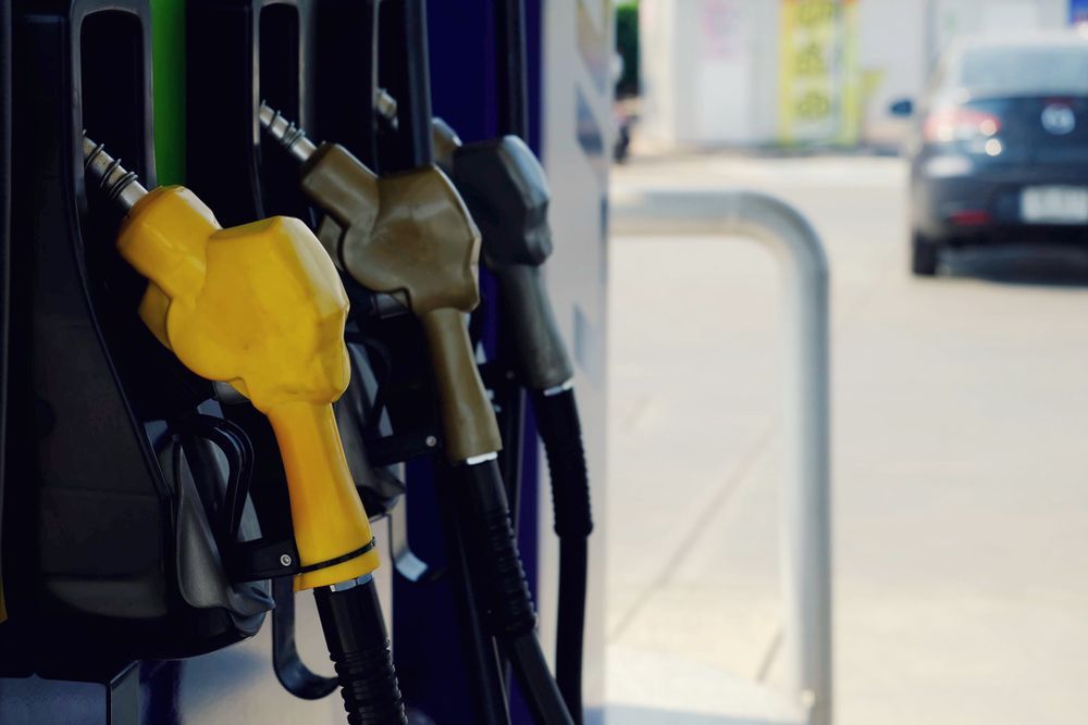 Gasoline pump nozzles in yellow, green, and gray, with a car in the background at a gas station.