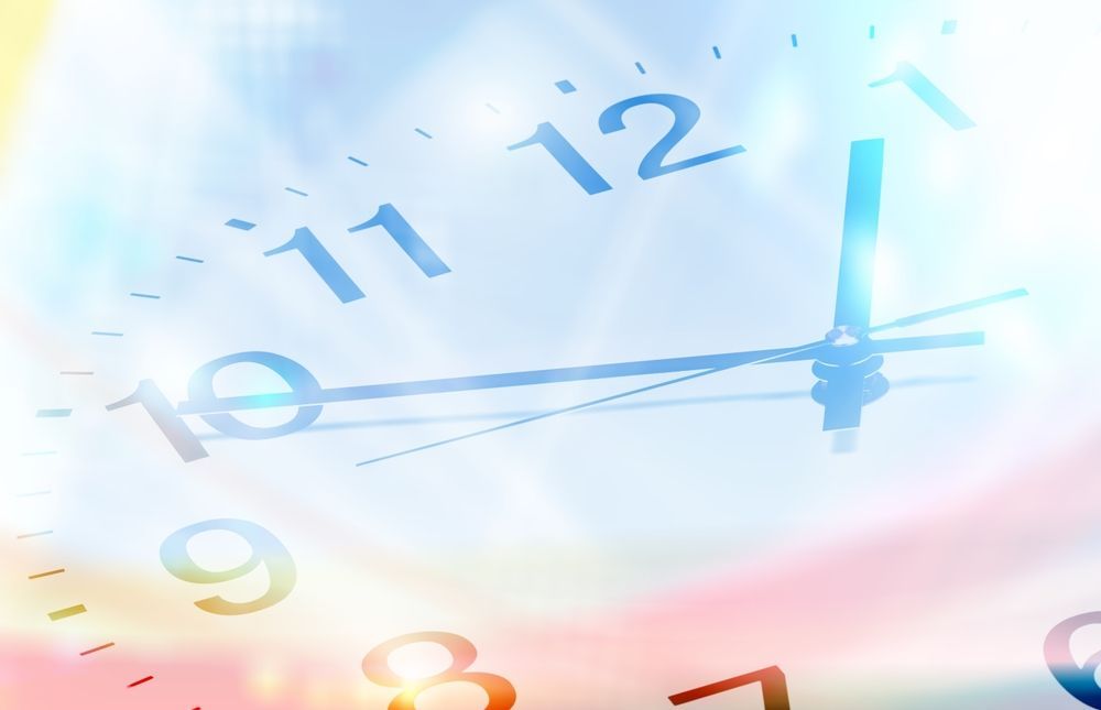 Clock face with blue hands, blurred background, time nearing 1 o'clock.