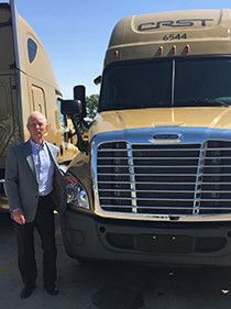 Man in suit stands beside a gold CRST semi-truck.