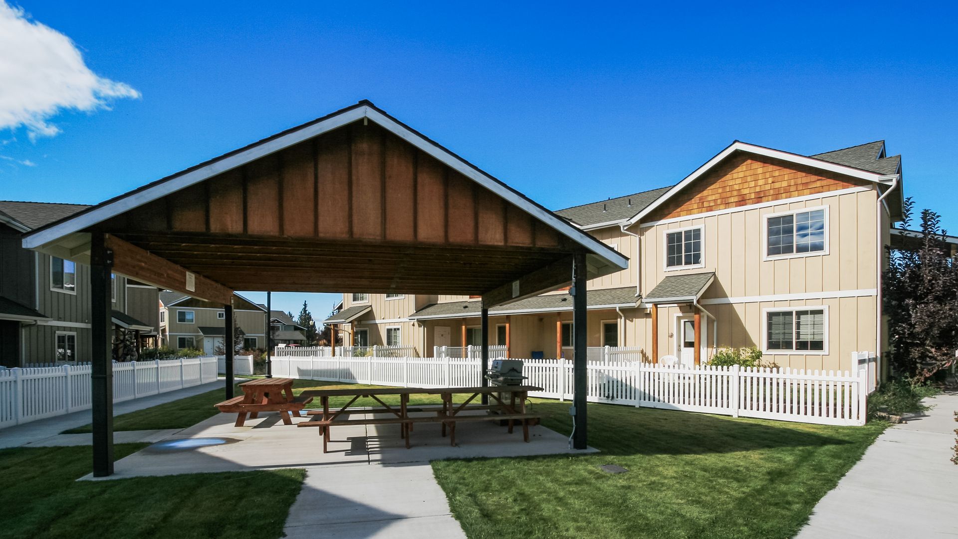 There is a picnic table under a gazebo in front of a house.