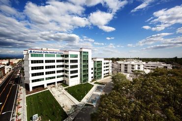 Exterior view of a bright modern medical center under a blue sky, with surrounding streets and trees.