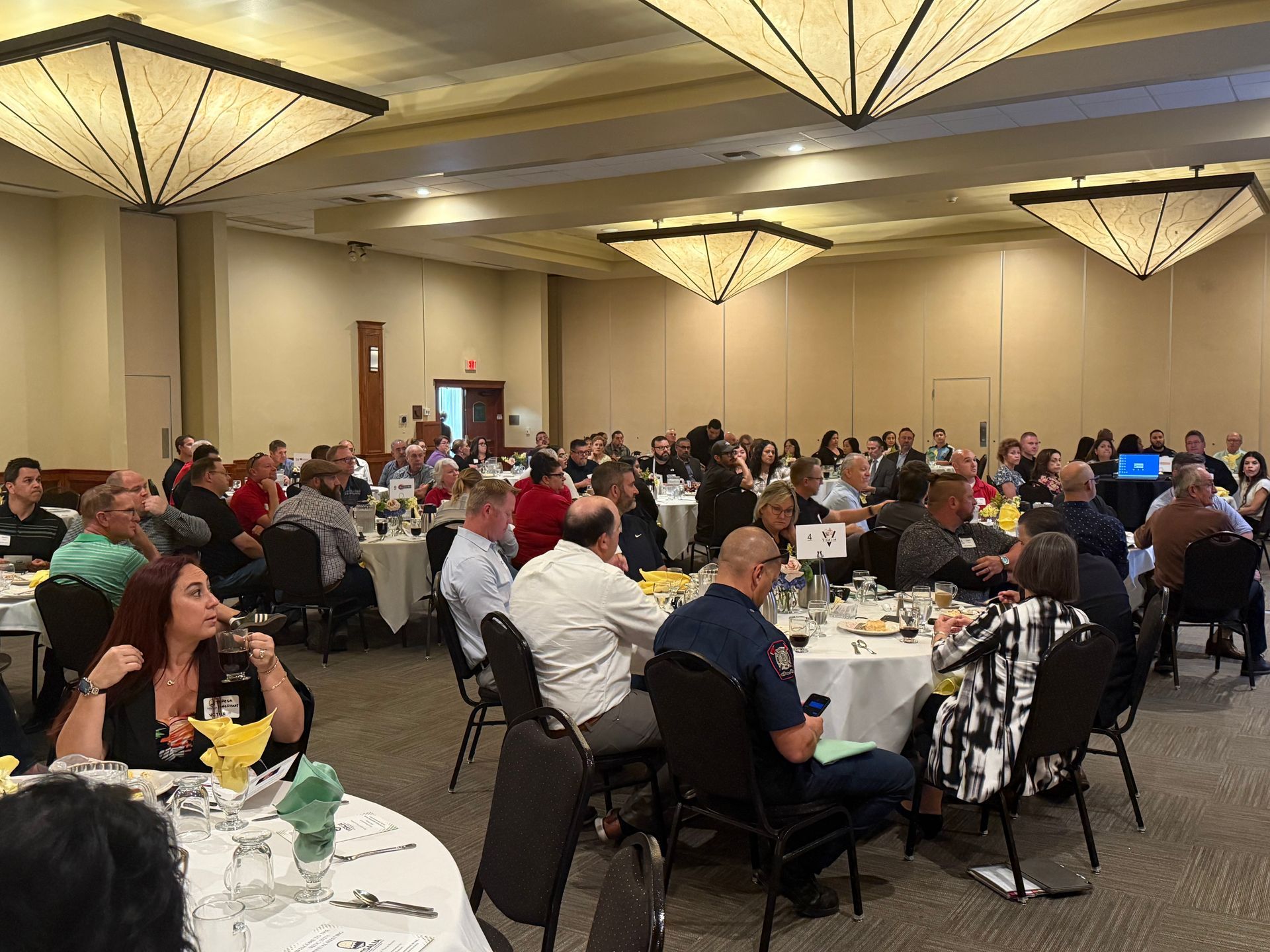 Large group of people seated at round tables in a banquet hall, presumably attending an event.