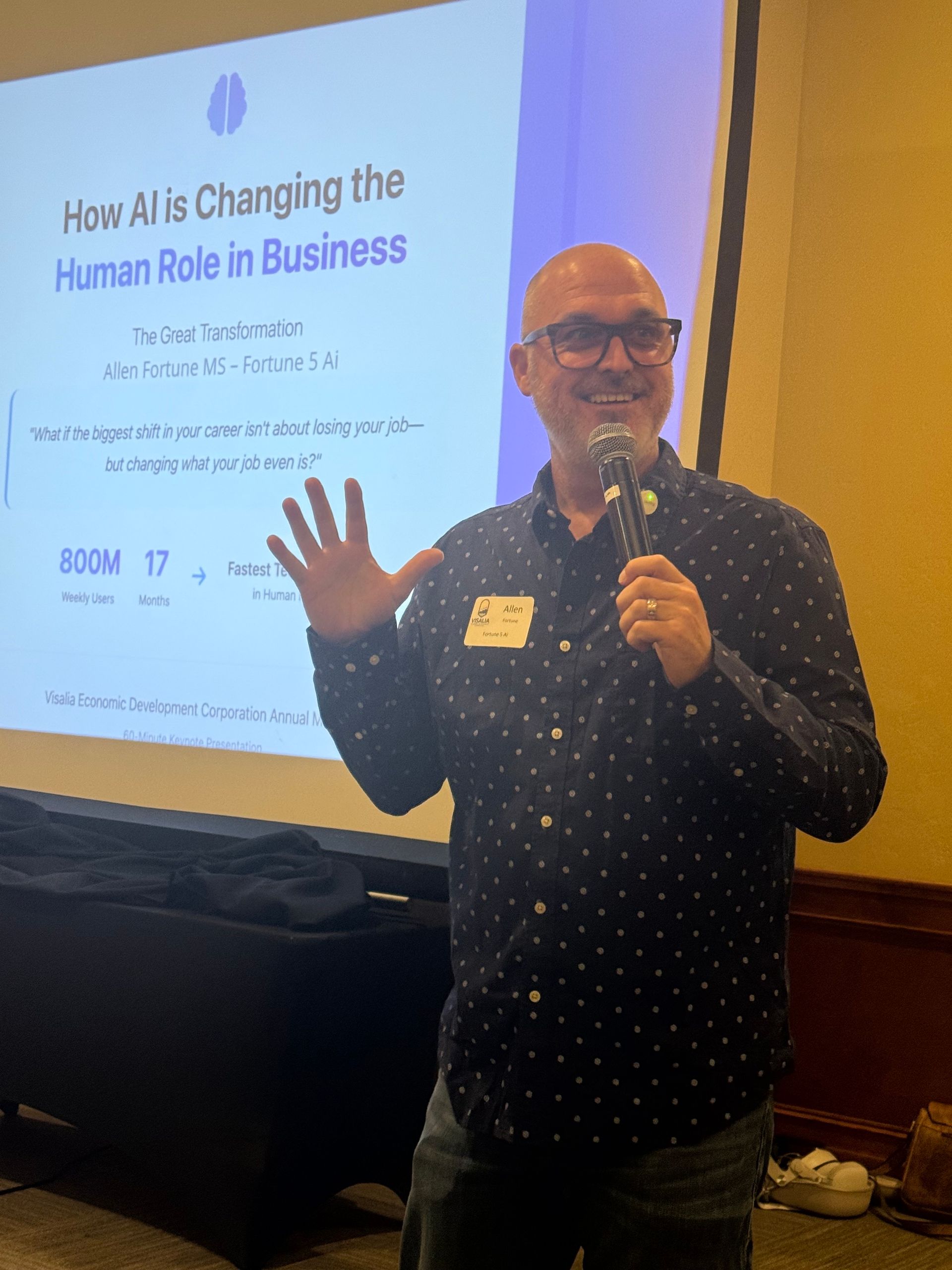 Man giving a presentation about AI in business, gesturing towards a screen with text, holding a microphone.