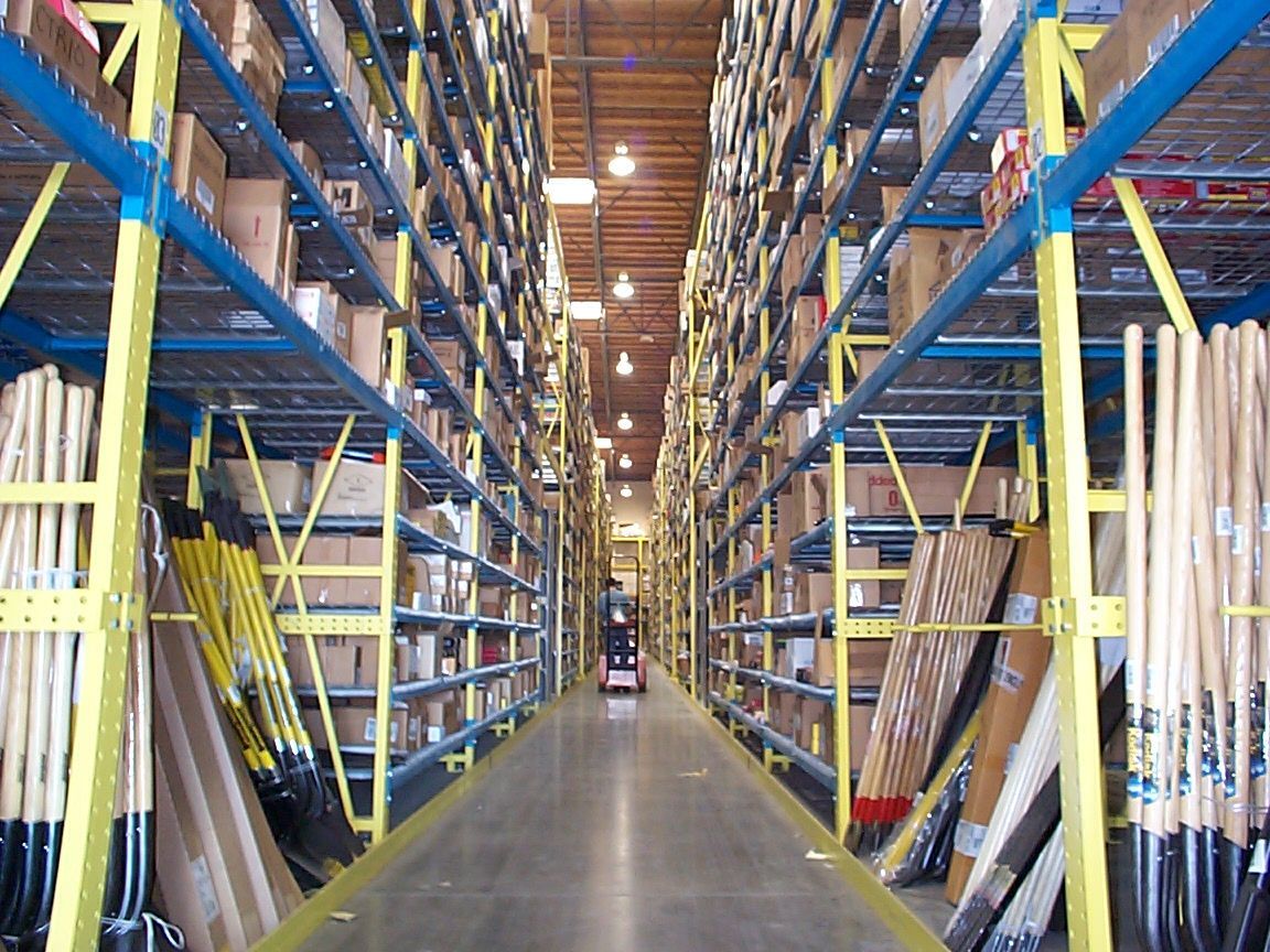 Warehouse interior with rows of shelves filled with boxes and items, forklift in aisle.