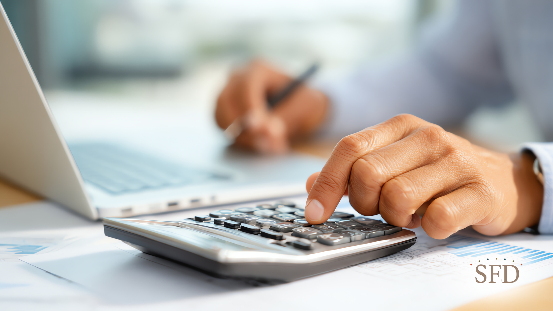 Person calculating with a calculator, laptop open, working with financial documents.