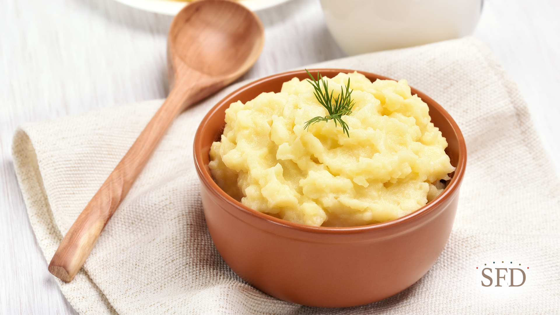 A bowl of mashed potatoes with a wooden spoon next to it.