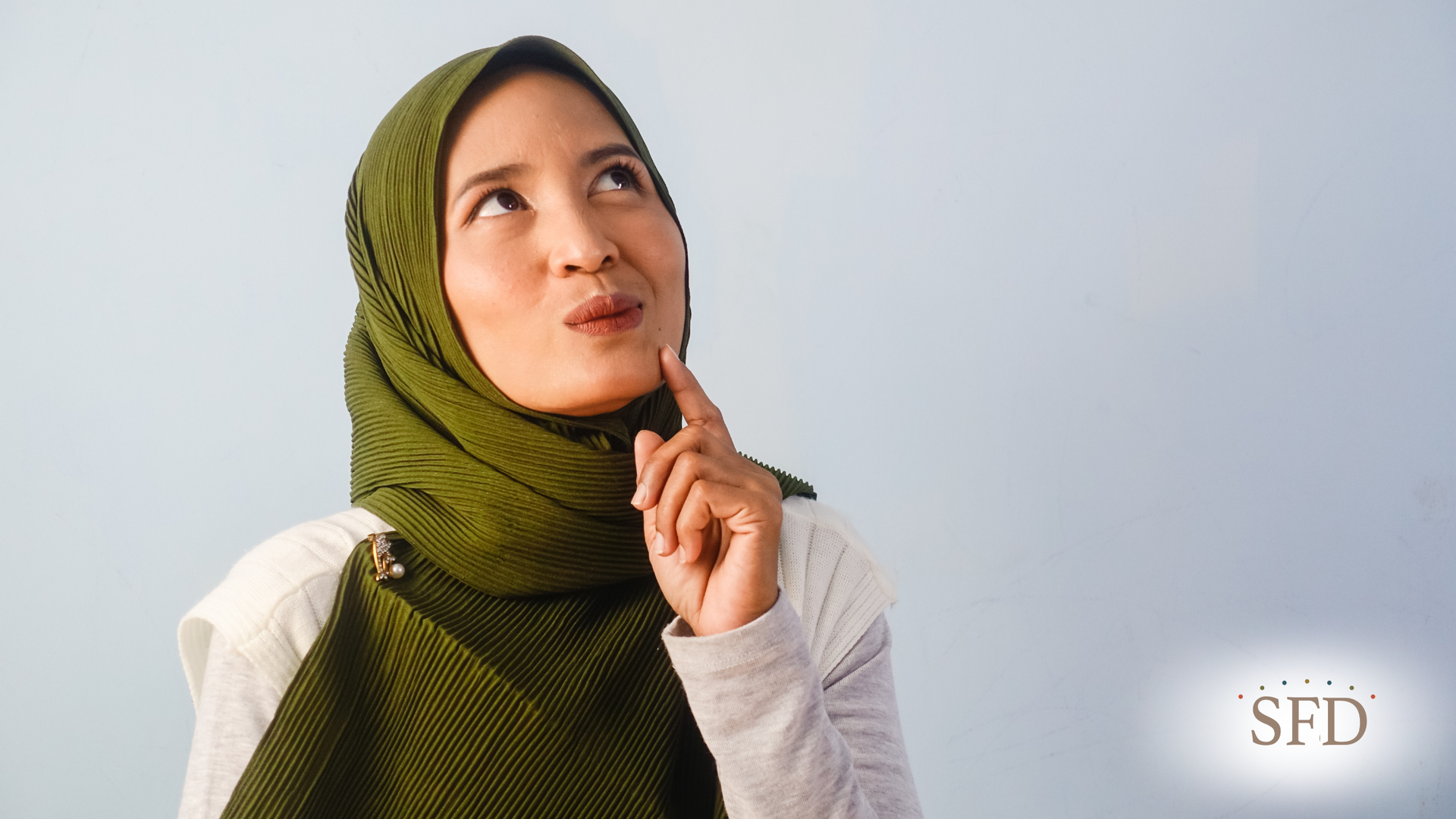 A woman wearing a green hijab and a white shirt is looking up.