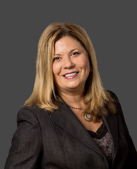 A woman in a suit and necklace is smiling for the camera.