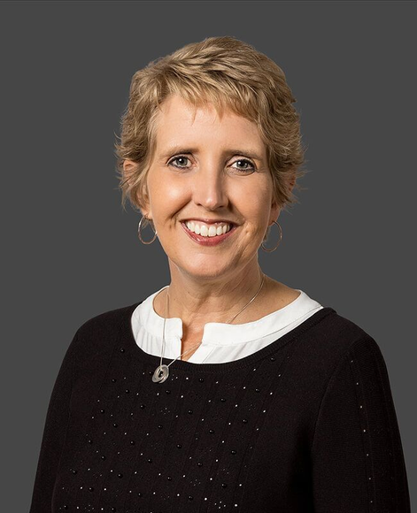 A woman in a black sweater and white shirt is smiling for the camera.