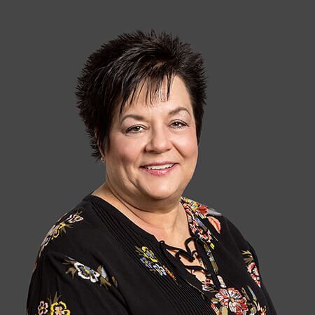 A woman in a black floral shirt is smiling for the camera.