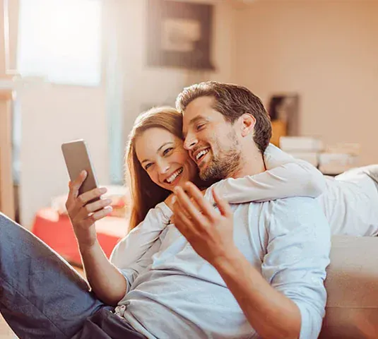 A couple sitting on a couch looking at a cell phone