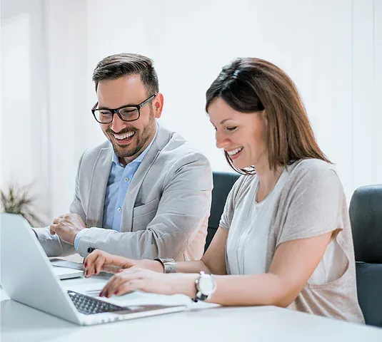 A man and a woman sitting at a table using a computer