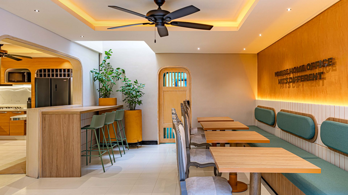Interior de cafetería con mesas, sillas y barra. Predominan los colores beige y verde. La luz del sol entra a raudales.