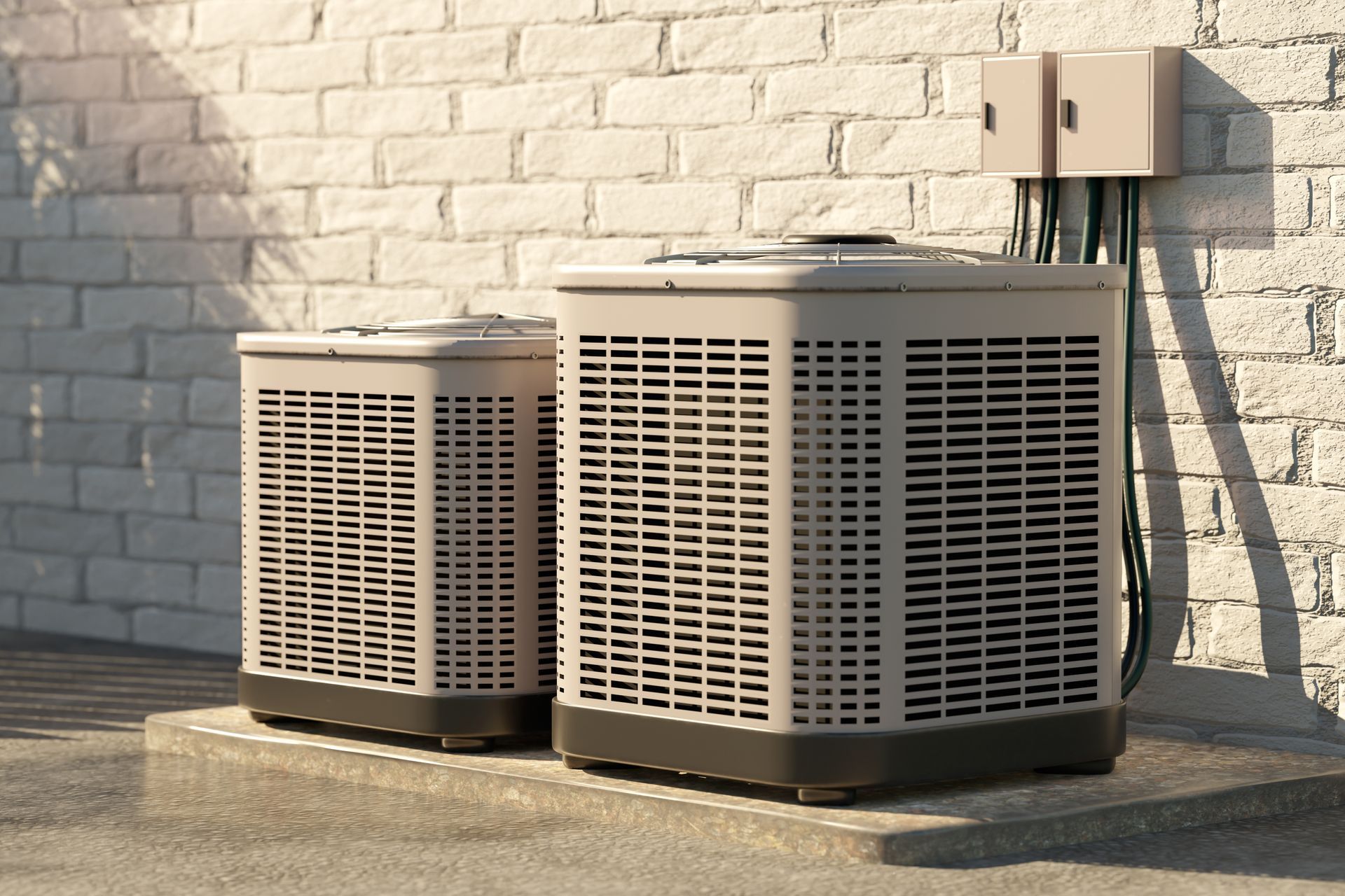 Two air conditioning units outdoors, next to a brick wall with electrical boxes and wiring.