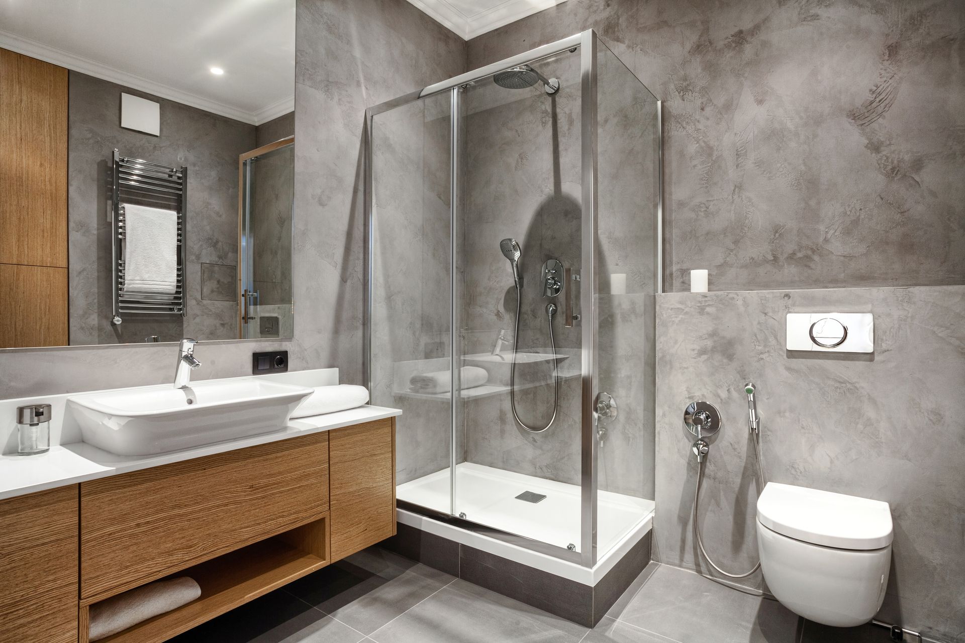 Modern bathroom with gray walls, glass shower, wooden vanity, and white toilet.