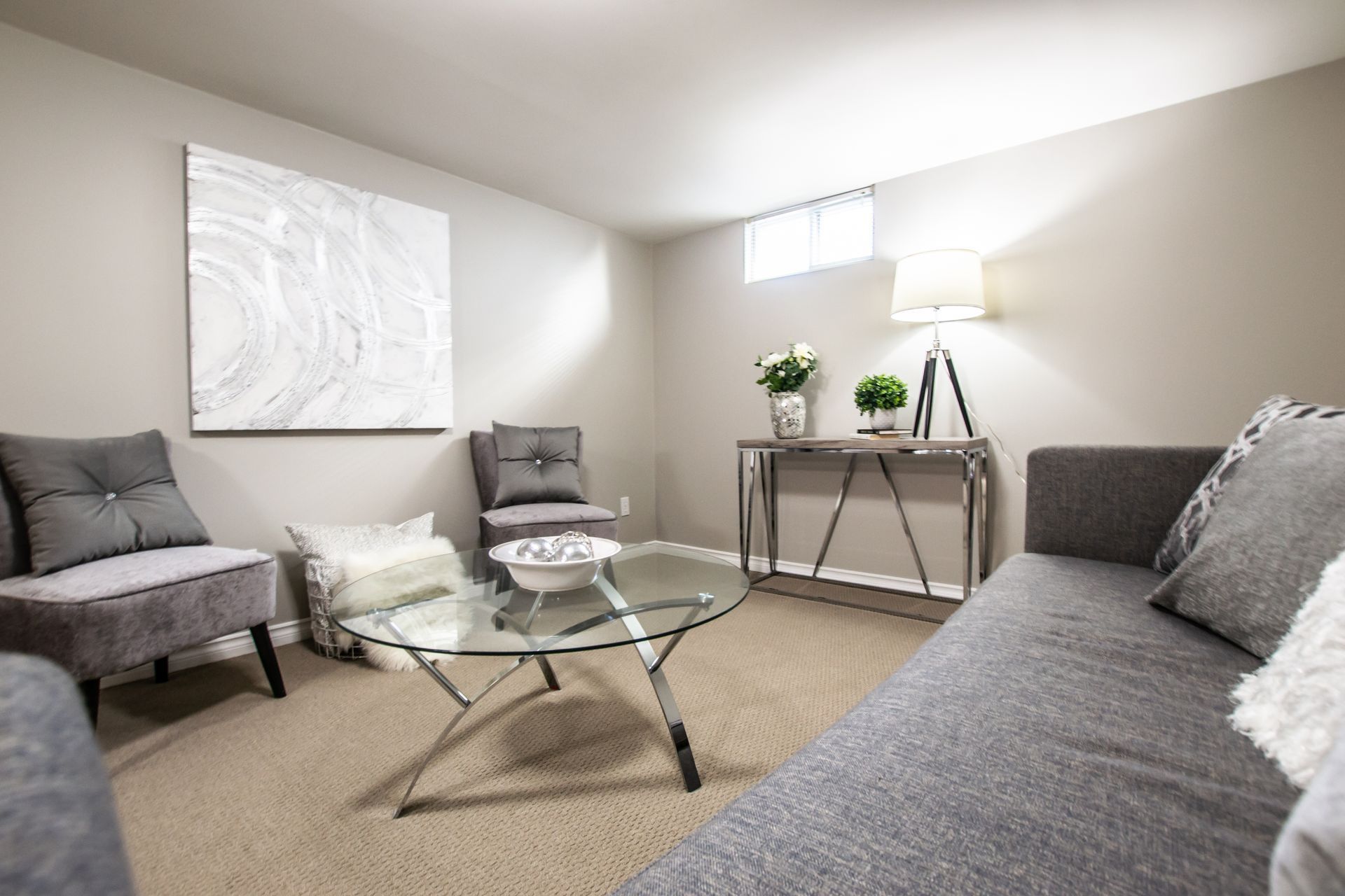 Gray living room with a sofa, chairs, glass coffee table, and artwork.