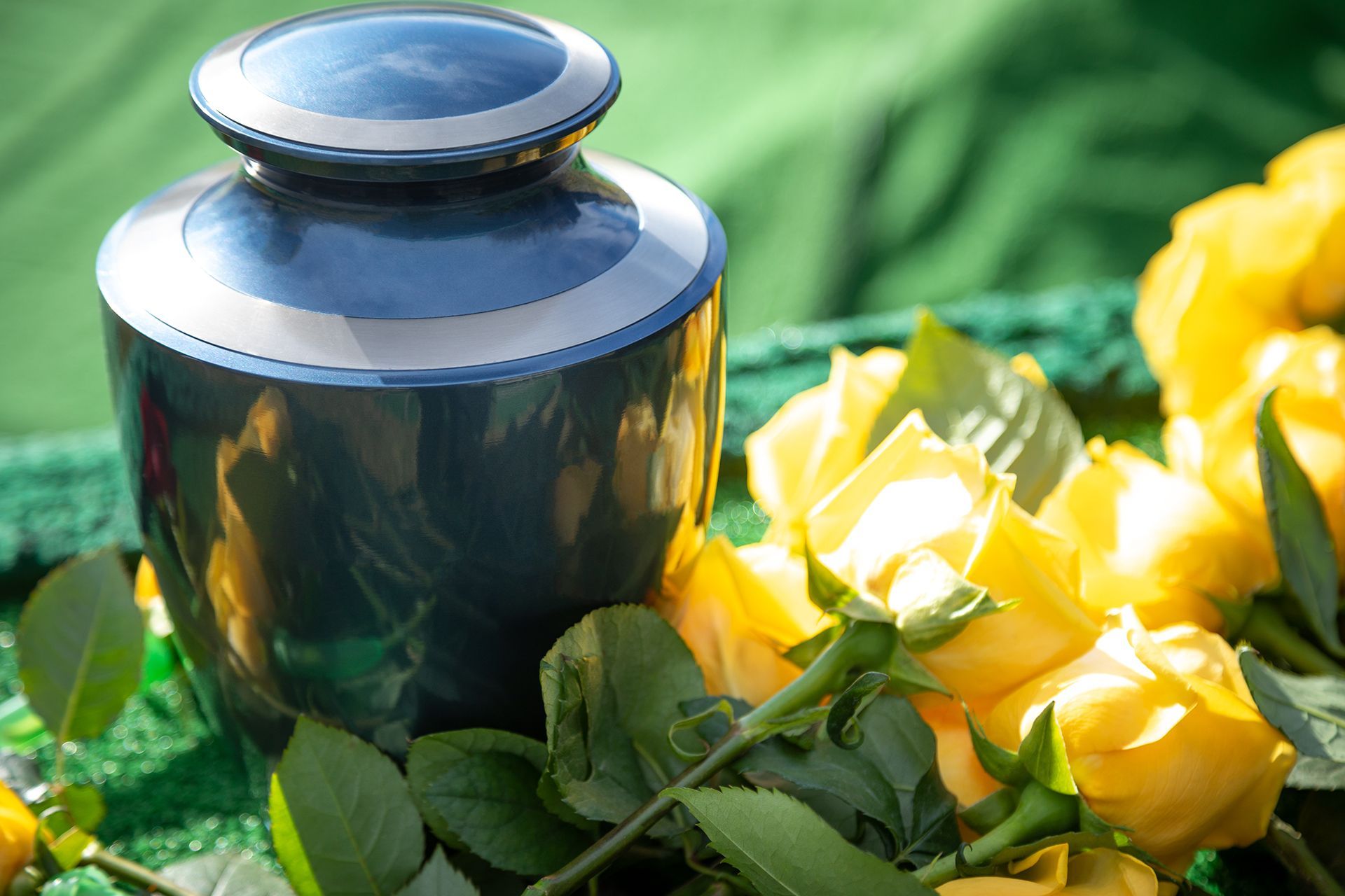 Blue cremation urn with yellow roses on a green surface.