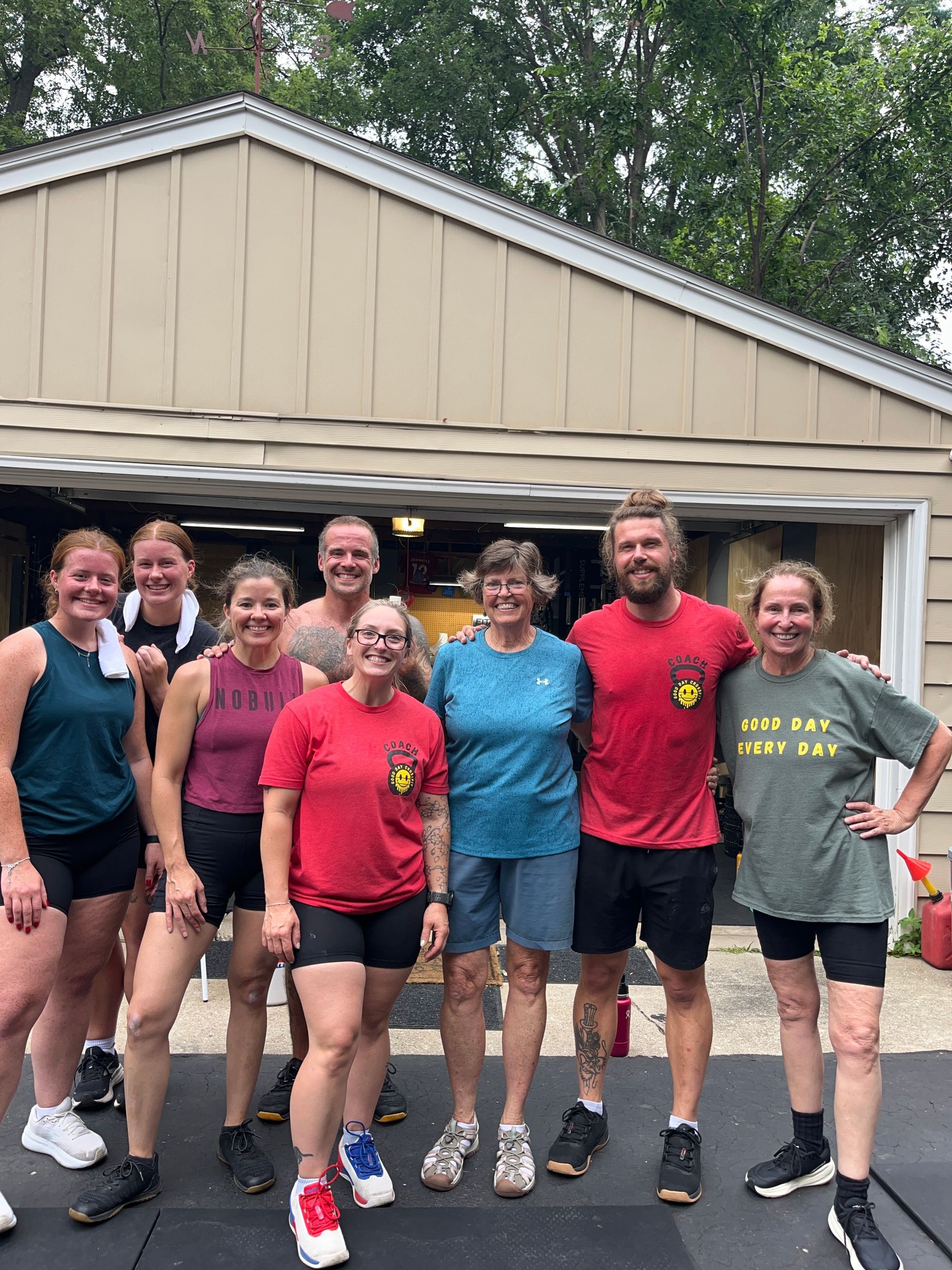 Group of CrossFitters posing together in front of a garage, smiling after a workout.