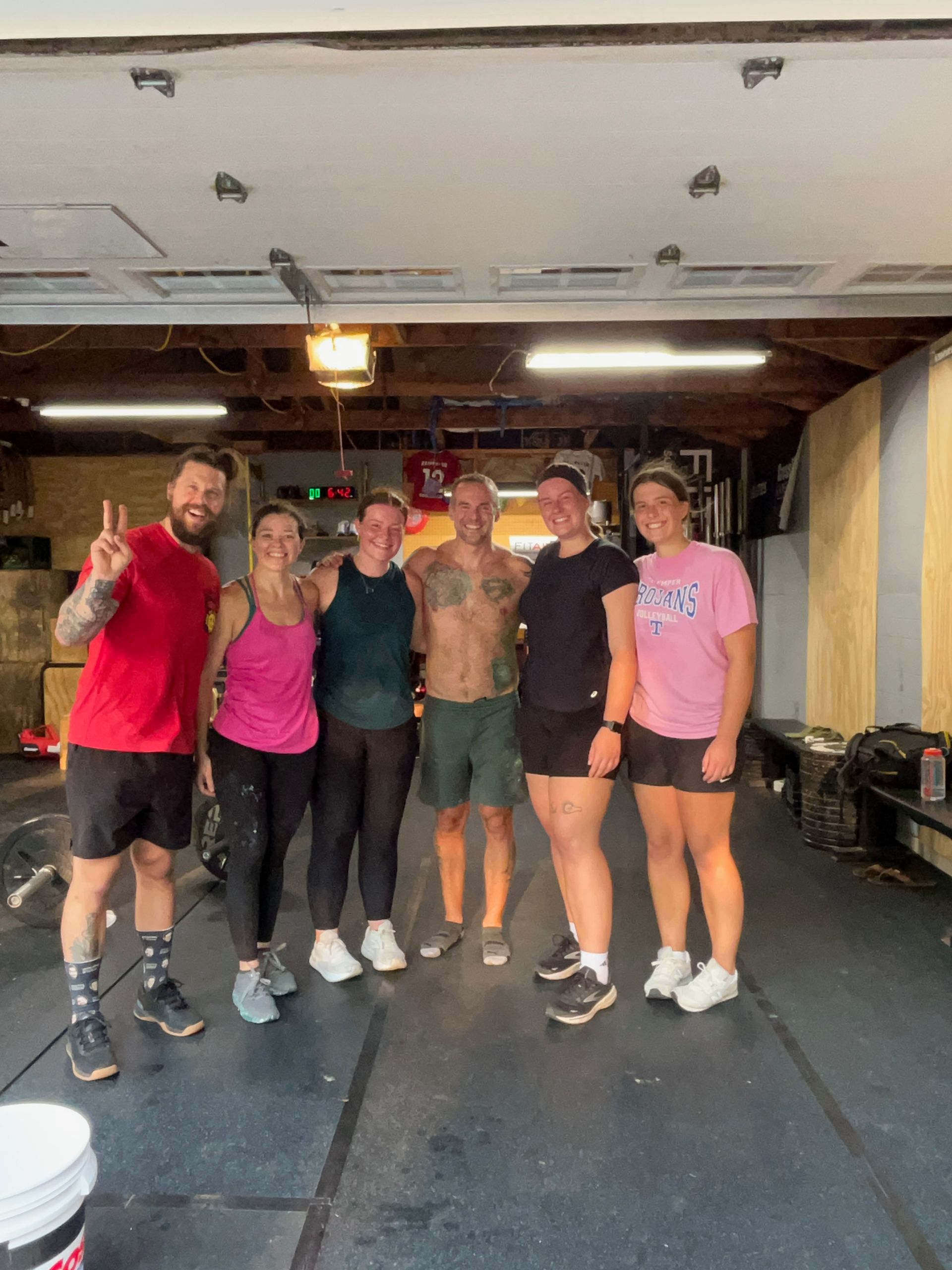 Five people posing together in a gym, smiling and raising their hands in a fitness class.