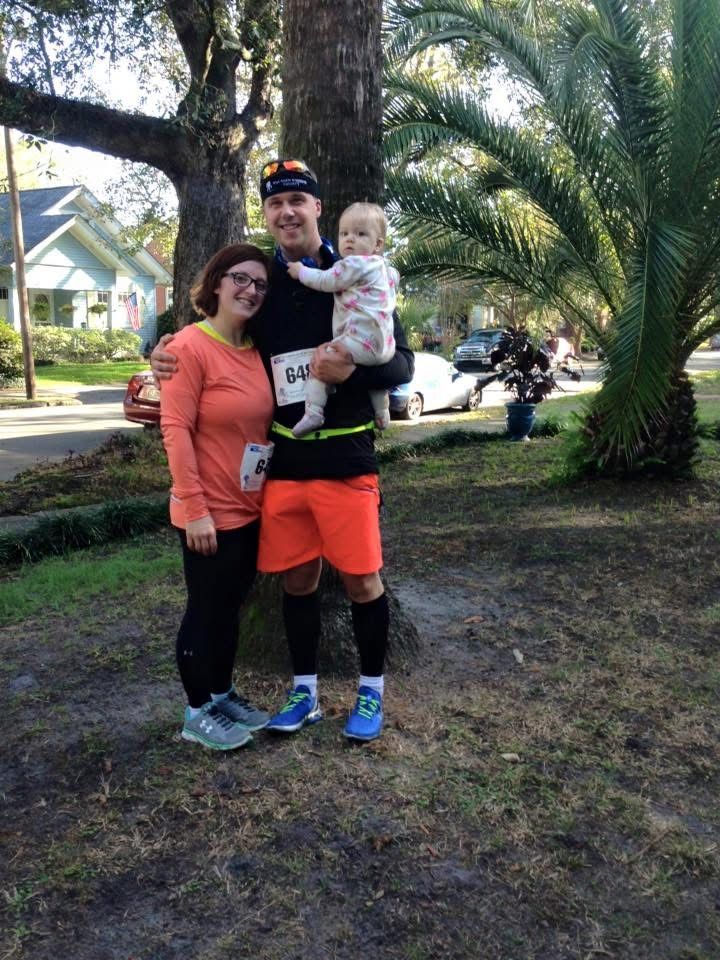 Two adults posing with a small child outdoors near palm trees, one in orange athletic wear.