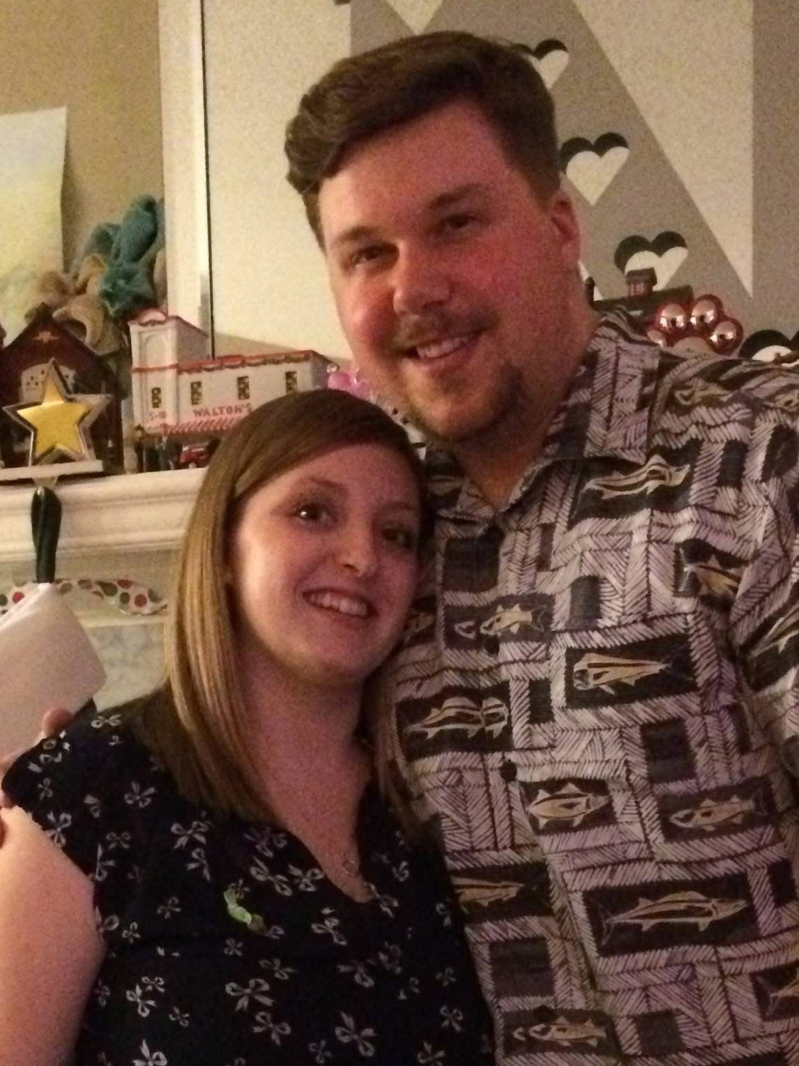Two people smiling and posing indoors, with heart decorations in the background.